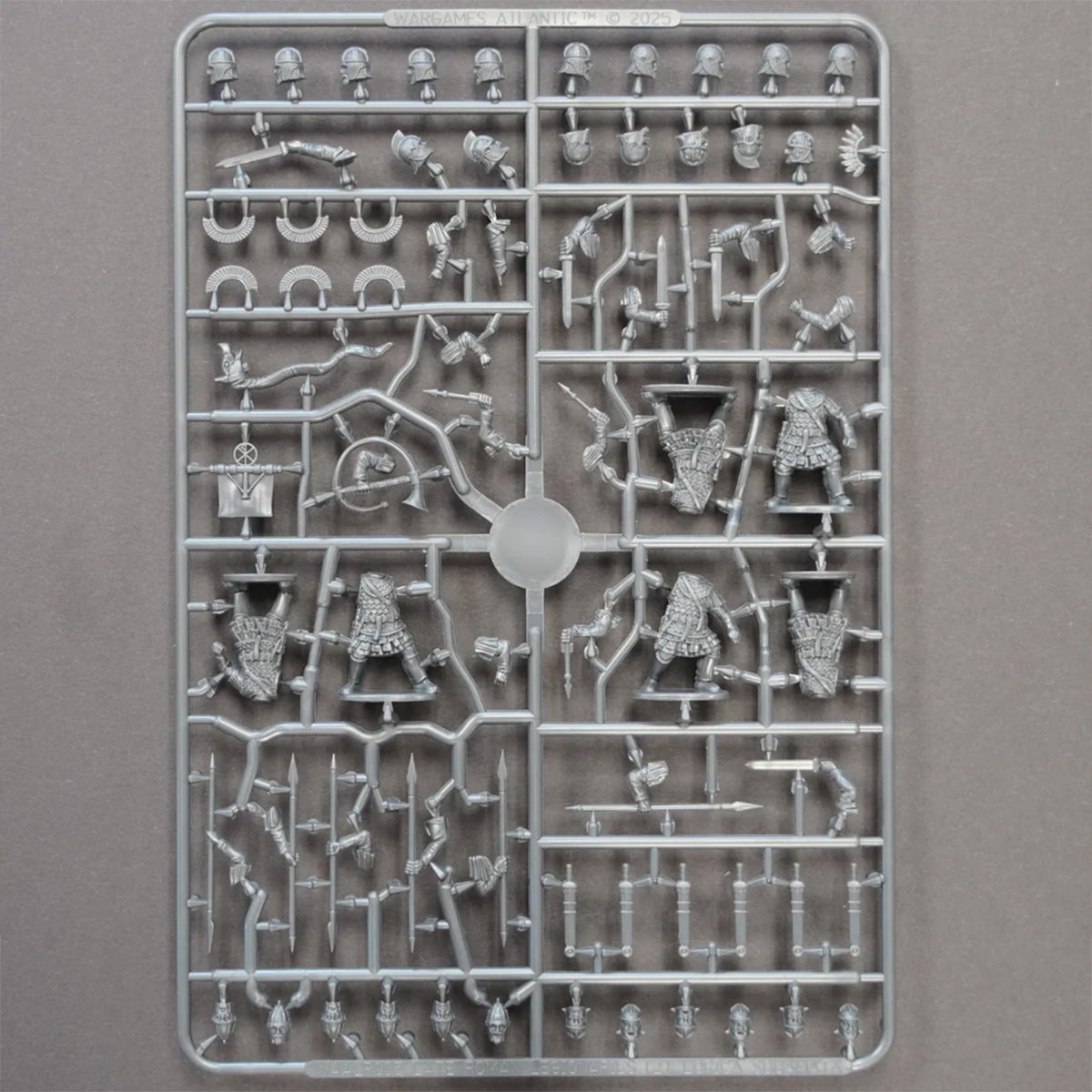 A gray plastic sprue containing unpainted Roman miniature figurines and accessories, photographed flat against a neutral gray background.