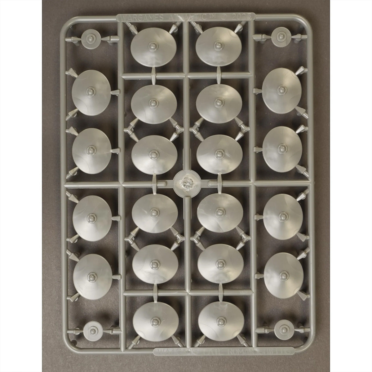 A rectangular gray plastic sprue holding multiple Roman shields, photographed from above on a plain taupe background.